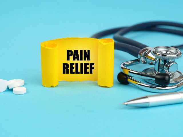 Medical concept. On a blue surface, a stethoscope, pills, a pen and a yellow sign with the inscription - PAIN RELIEF