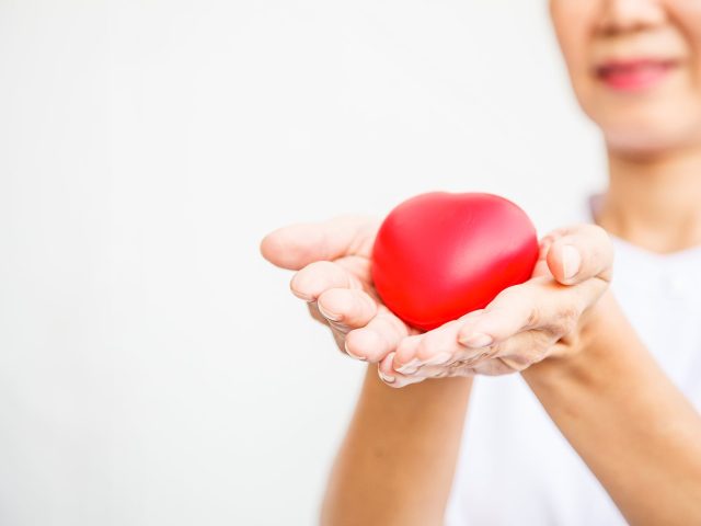 Selective Focus Of Red Heart Held By Smiling Female Nurse's Both